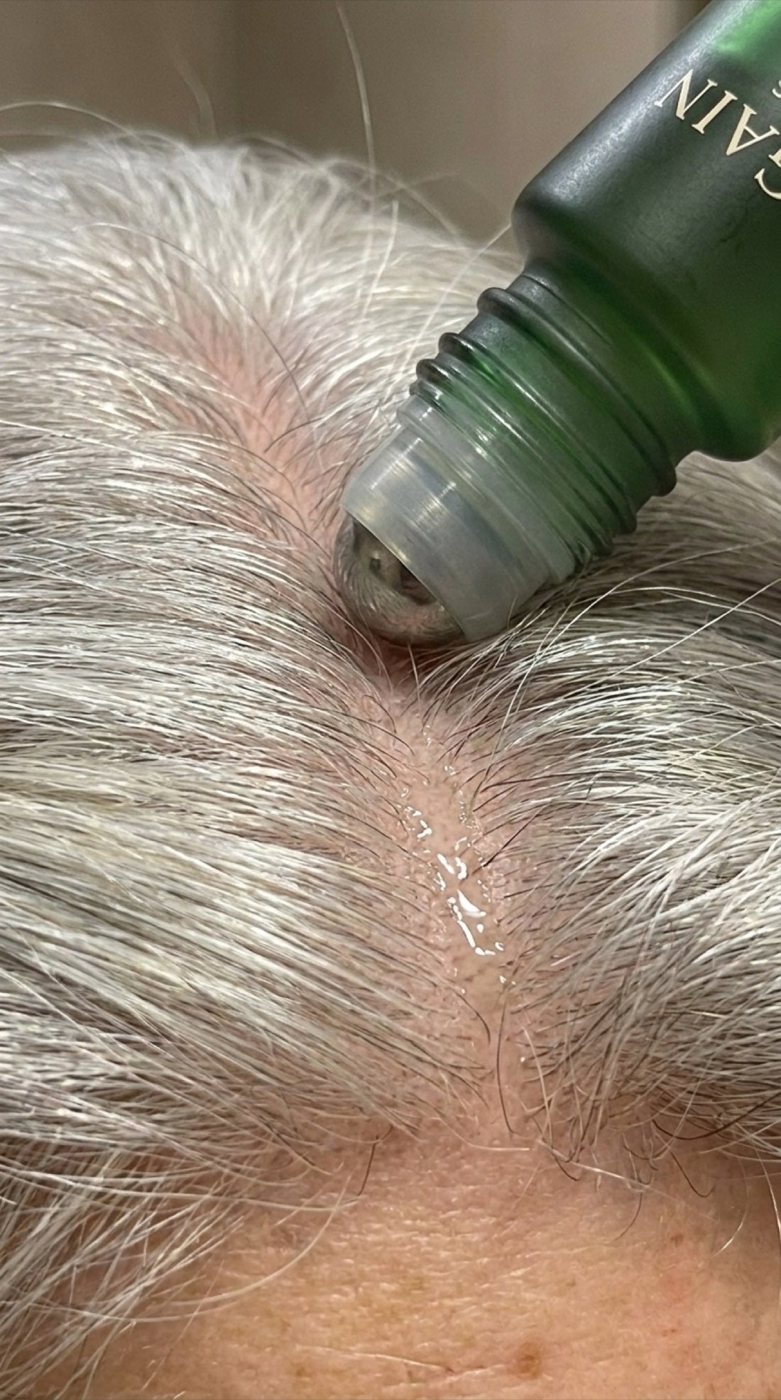 Gros plan sur la bille acier du roll-on qui masse le cuir chevelu à la racine des cheveux argentés